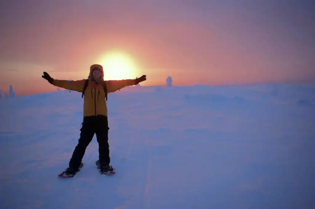A person snowboarding at sunset in snowy Lapland with arms outstretched.