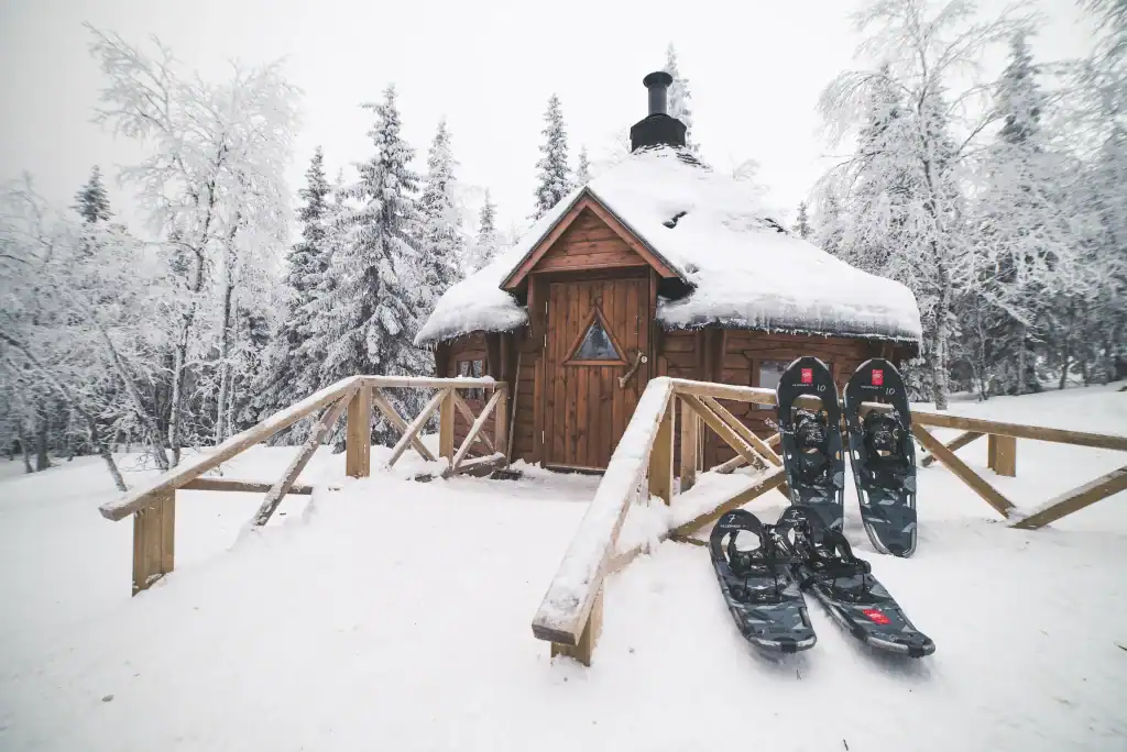Cozy wooden cabin in snowy forest with snowshoes outside in Ylläsjärvi, Lapland.