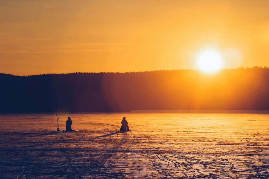 A stunning sunset over a snowy landscape with two people ice fishing.