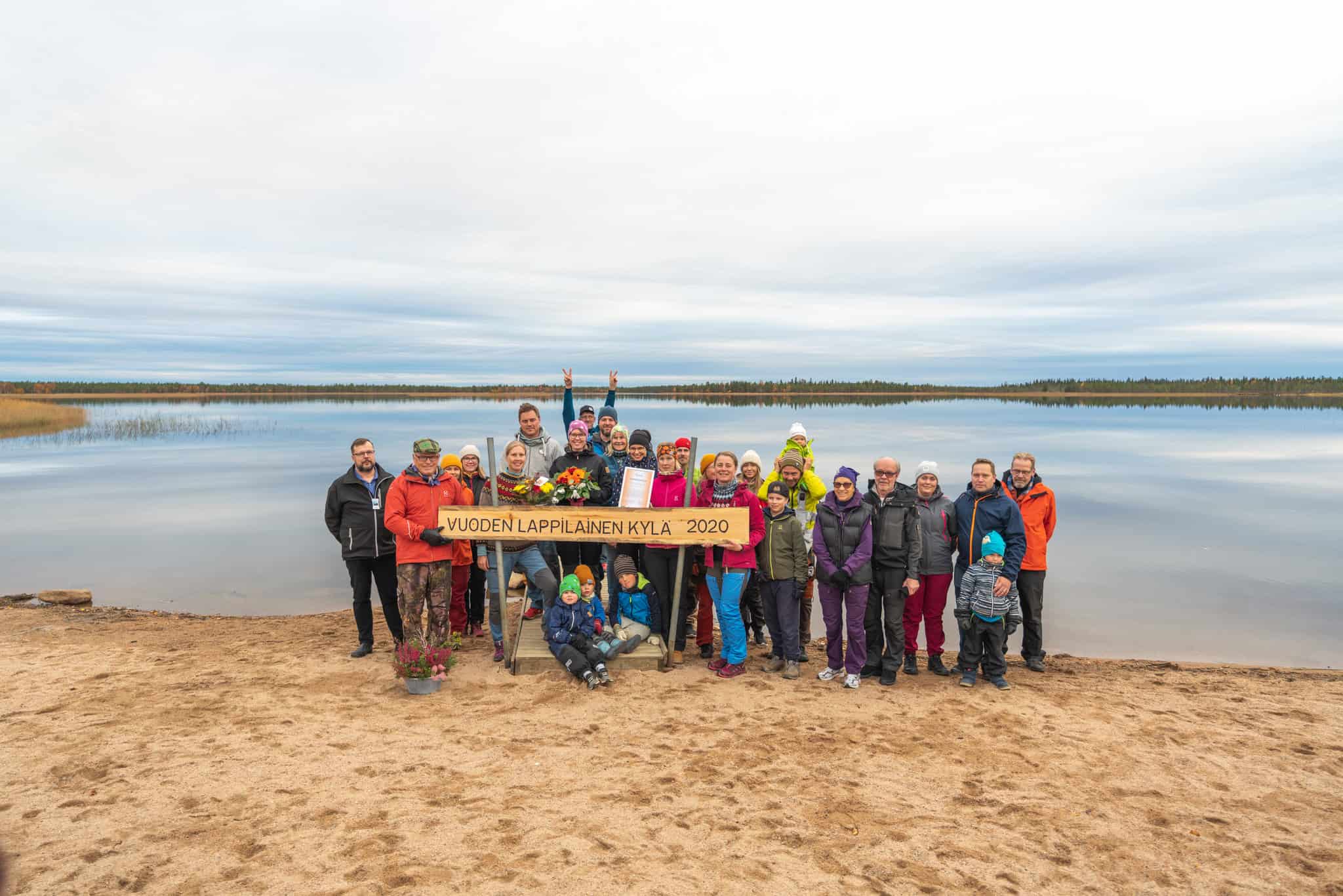 Group of tourists holding a banner on the sandy shore of Ylläsjärvi lake in Lapland, Finland, during.