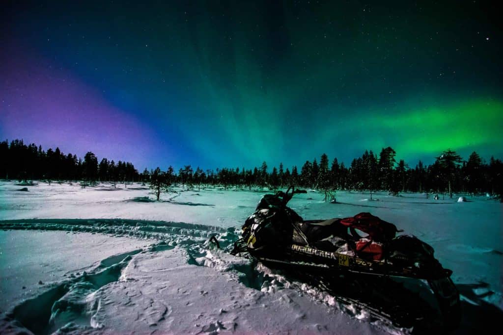 Aurora borealis over snowy landscape with snowmobile in Finnish Lapland.