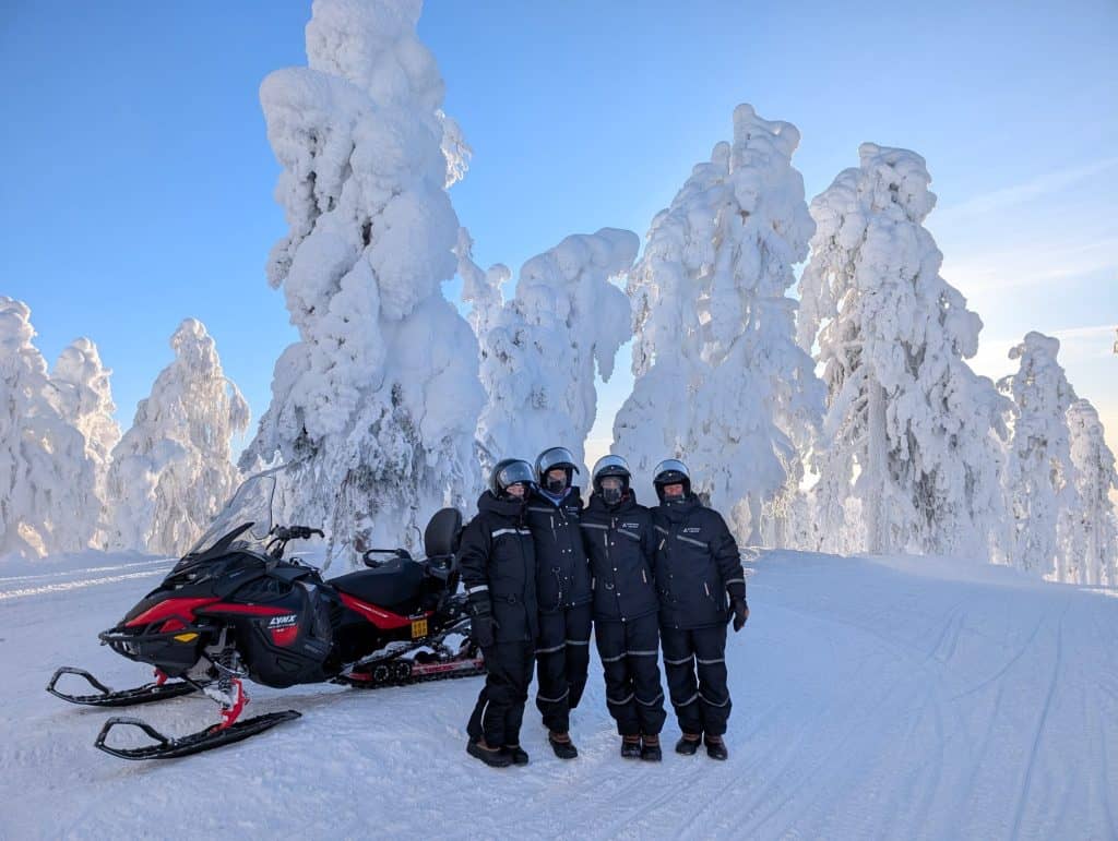 Groupe de motoneige dans la neige de la Lapland enneigée, avec des arbres glacés en arrière-plan.