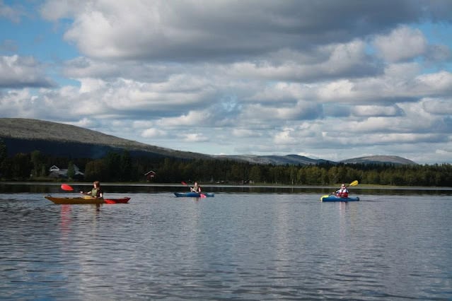 Kayakers paddling on calm Ylläsjärvi Lake under a partly cloudy sky in Finnish Lapland.