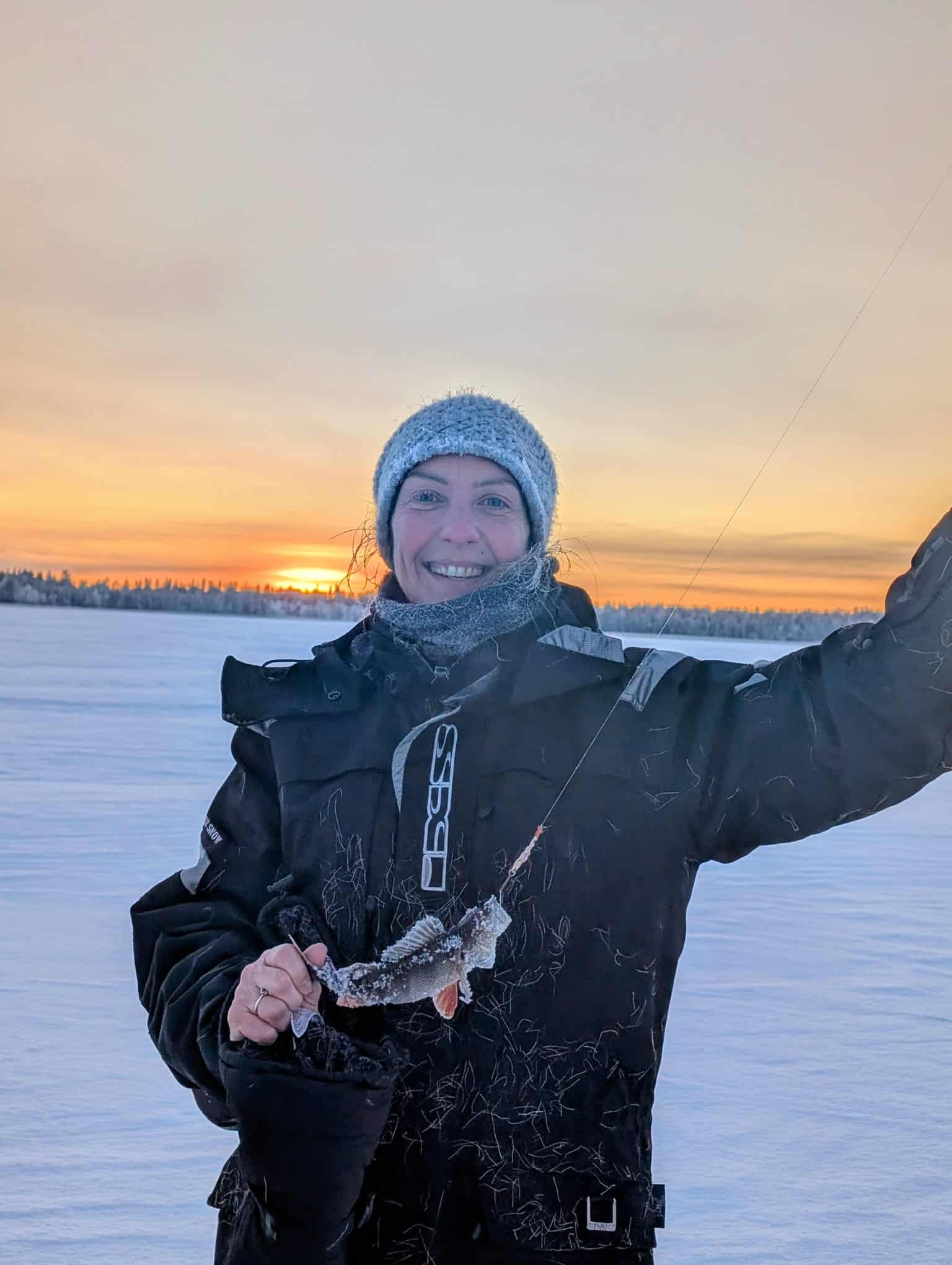 Guests sitting on reindeer skins while ice fishing on Lake Ylläsjärvi