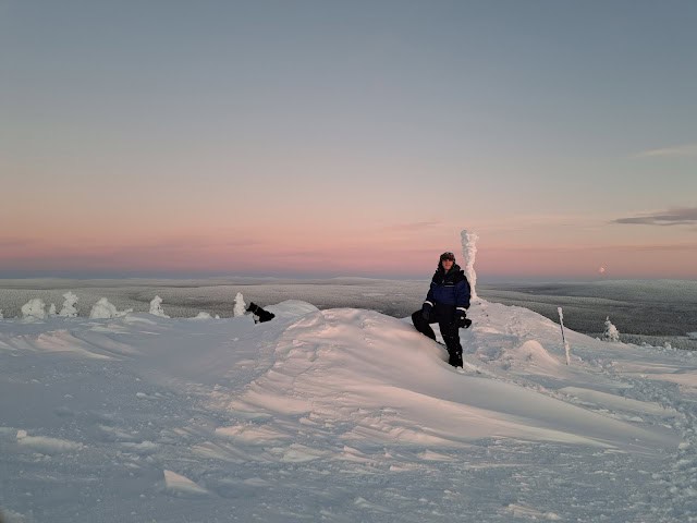Sunset over snowy Arctic terrain with a person sitting on a snowbank at dusk.