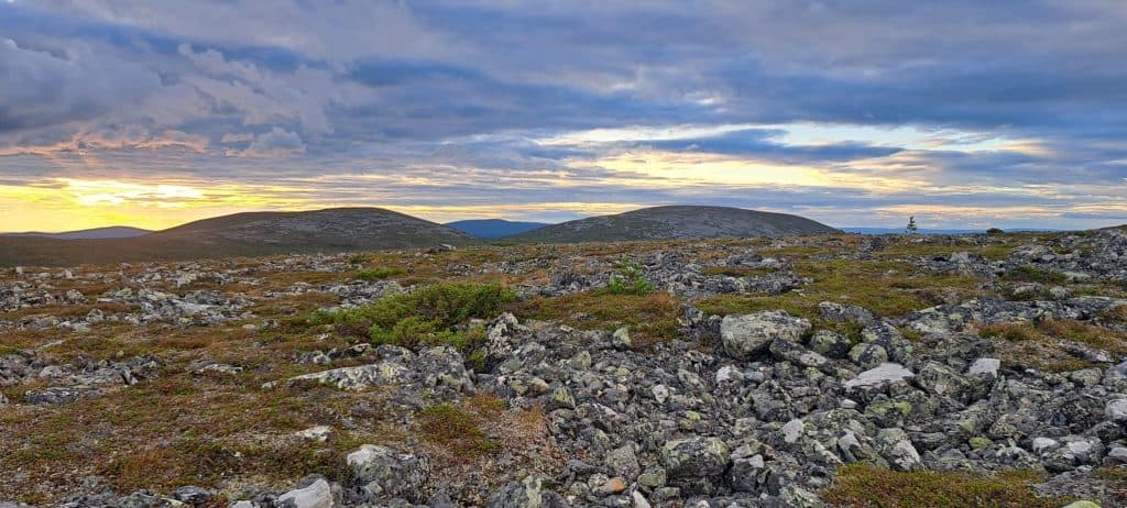 Aurora borealis over rocky Arctic landscape in Finnish Lapland at dusk.
