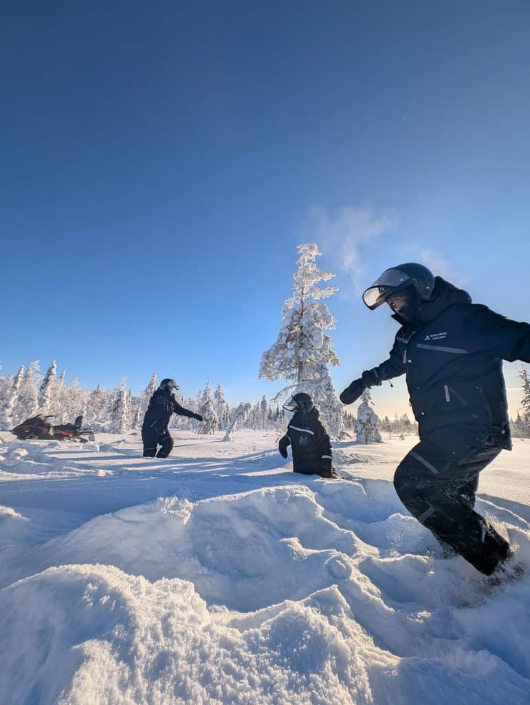 Family enjoying snowshoeing in snowy Lapland under clear blue sky.